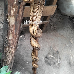 Könnte beinhalten: Handgeschnitzter Holz-Spazierstock in Form einer Kobra. Der Schlangenkopf ist mit aufwendigen Mustern versehen, und der Körper windet sich entlang des Stocks. Der Text "afridugah" ist auf dem Stock zu sehen.