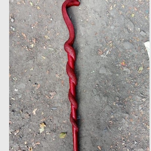 May include: A red walking cane with a snake design. The cane is a deep red color, with the body of a snake wrapped around the shaft. The snake's head forms the handle, and the cane is made of wood.