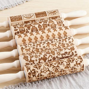 May include: Six wooden rolling pins with festive Christmas patterns. Each pin has a light wood finish, white handles, and engraved designs such as gingerbread men, snowflakes, and Santa Claus. The rolling pins are ideal for baking.