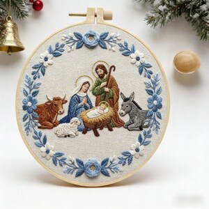 Può includere: Scena della Natività natalizia ricamata in un cerchio. La scena raffigura Maria, Giuseppe e Gesù bambino, circondati da animali. Il cerchio è decorato con ricami floreali blu e bianchi. Una campana d'oro e del verde sono sullo sfondo.