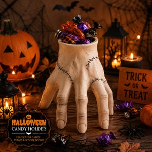 May include: A beige, hand-shaped candy bowl featuring dark, stitched-like markings across the fingers and palm. The hollow, upright hand serves as a container, currently filled with various colorful, individually wrapped Halloween candies.