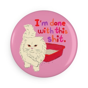 Könnte beinhalten: Ein pinkfarbener Button mit dem Text "I'm done with this shit" in bunten Farben. Eine Cartoon-Katze mit wütendem Blick steht neben einer roten Katzentoilette.