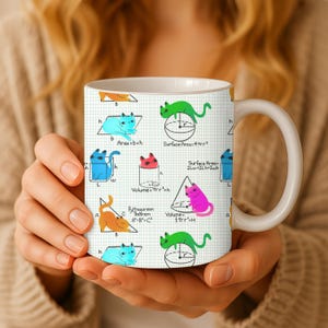 May include: White ceramic mug featuring a repeating pattern of colorful cartoon cats and geometric formulas on a grid background. The mug includes formulas for area, volume, and the Pythagorean theorem.