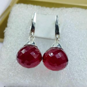 Puede incluir: Un par de pendientes de plata con piedras preciosas rojas oscuras facetadas en forma de lágrima. Los pendientes tienen un diseño sencillo y elegante, con un lazo y una tapa de plata.