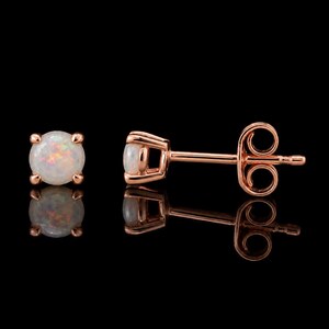 May include: A pair of stud earrings featuring round, iridescent white opals set in rose gold metal. One earring is shown from the front, while the other is displayed from the side, revealing the post and the secure butterfly back mechanism.