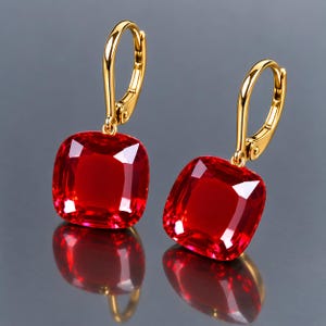 May include: A pair of drop earrings featuring large, square-cut, vibrant red gemstones with rounded corners. The stones are set in polished gold-tone metal with secure lever-back closures, reflecting light to showcase their deep crimson color.