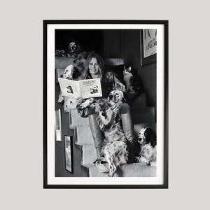 Puede incluir: Fotograf&iacute;a enmarcada en blanco y negro de una persona leyendo un libro en una escalera, rodeada de varios perros y un gato. La portada del libro muestra el t&iacute;tulo "Woof Woof". La imagen es un retrato.