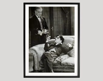 Fotogramma vintage di Charlie Chaplin, scena classica del cinema muto su un divano, fotografia cinematografica in bianco e nero, commedia senza tempo da appendere al muro.