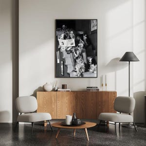 Puede incluir: Una impresi&oacute;n enmarcada en blanco y negro de una mujer leyendo un libro rodeada de perros. La impresi&oacute;n cuelga sobre un mueble de madera con una mesa de centro redonda y dos sillas grises. Tambi&eacute;n se ve una l&aacute;mpara de pie negra y velas.