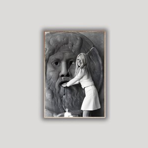 May include: A monochrome photograph featuring a woman in a white outfit touching a stone fountain sculpture of a bearded face. The image is framed within a wooden border.