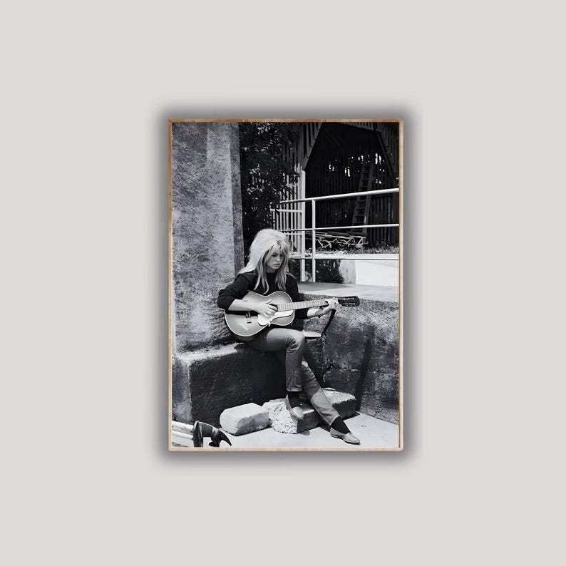 Pu&ograve; includere: Fotografia in bianco e nero di una donna che suona una chitarra acustica. &Egrave; seduta all'aperto, indossa una giacca scura e jeans. L'immagine ha un'estetica vintage, con un focus sulla musicista e il suo strumento.