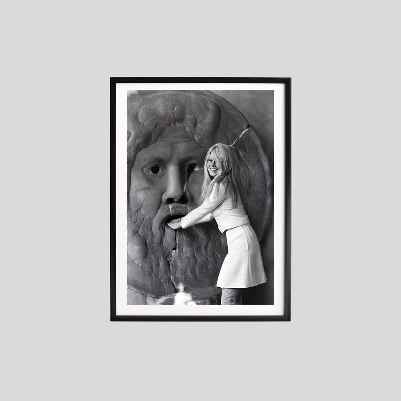 May include: Framed black and white photograph of a woman in a white outfit touching a stone sculpture of a face. The photograph is presented in a black frame.
