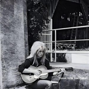 Pu&ograve; includere: Fotografia in bianco e nero di una persona che suona una chitarra acustica. La persona ha lunghi capelli chiari e indossa un top scuro. La chitarra &egrave; marrone chiaro con un battipenna bianco. Lo sfondo include un edificio e del fogliame.
