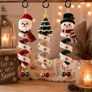 Peut inclure: Trois décorations suspendues en crochet représentant un père Noël, un sapin de Noël et un bonhomme de neige. Chaque figurine possède une longue queue blanche en spirale ornée de flocons brodés rouges et verts, terminée par des grelots.