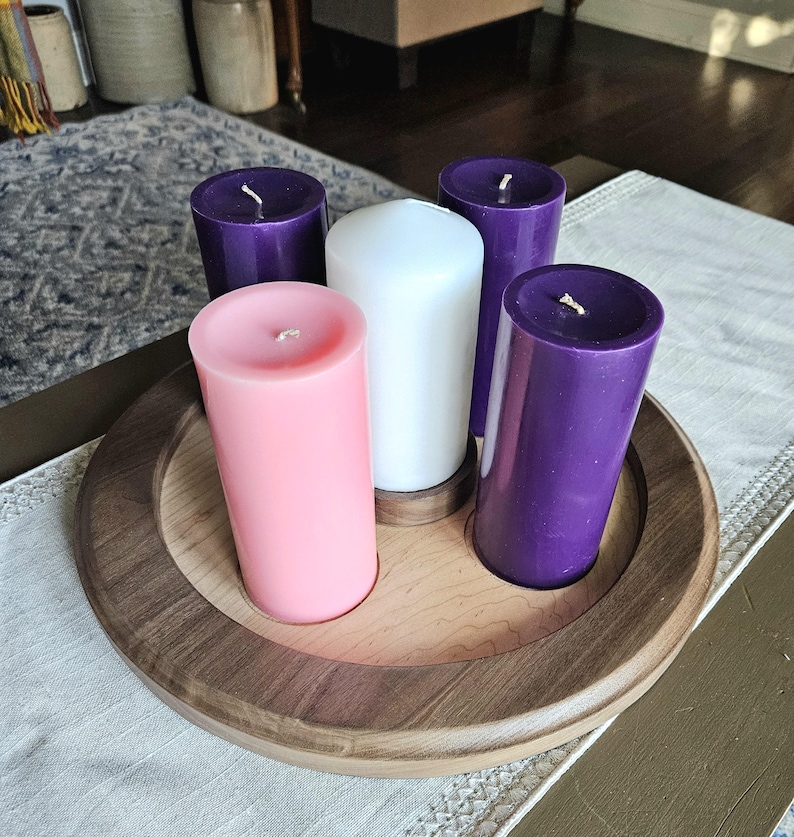 May include: A wooden candle holder with five pillar candles. The candles are pink, white, and purple. The holder is round with a dark brown rim and a lighter wood interior. The candles are unlit.