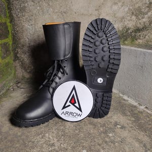 May include: Black leather combat boots with a lace-up design and a thick, lug sole. The boots are displayed with a round logo that reads "ARROW LEATHERS". The sole of one boot shows a size 9.