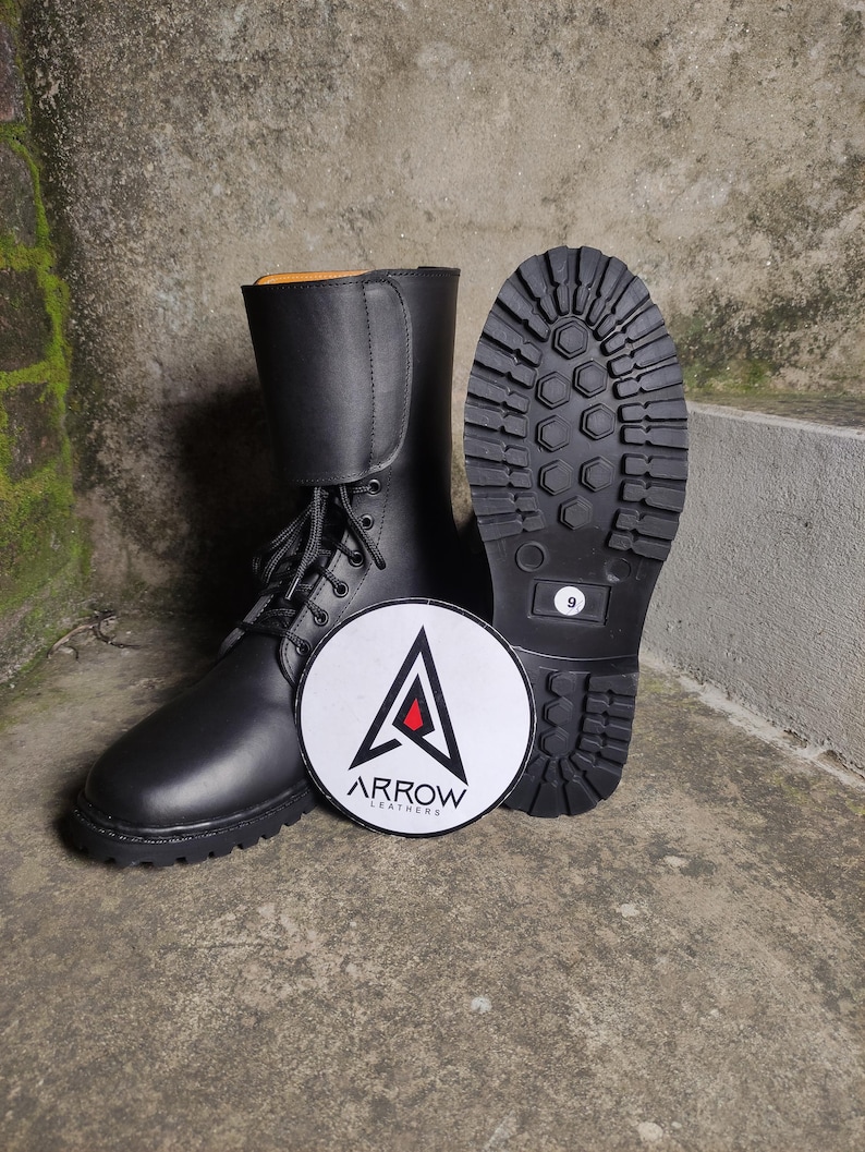 May include: Black leather combat boots with a lace-up design and a thick, lug sole. The boots are displayed with a round logo that reads "ARROW LEATHERS". The sole of one boot shows a size 9.