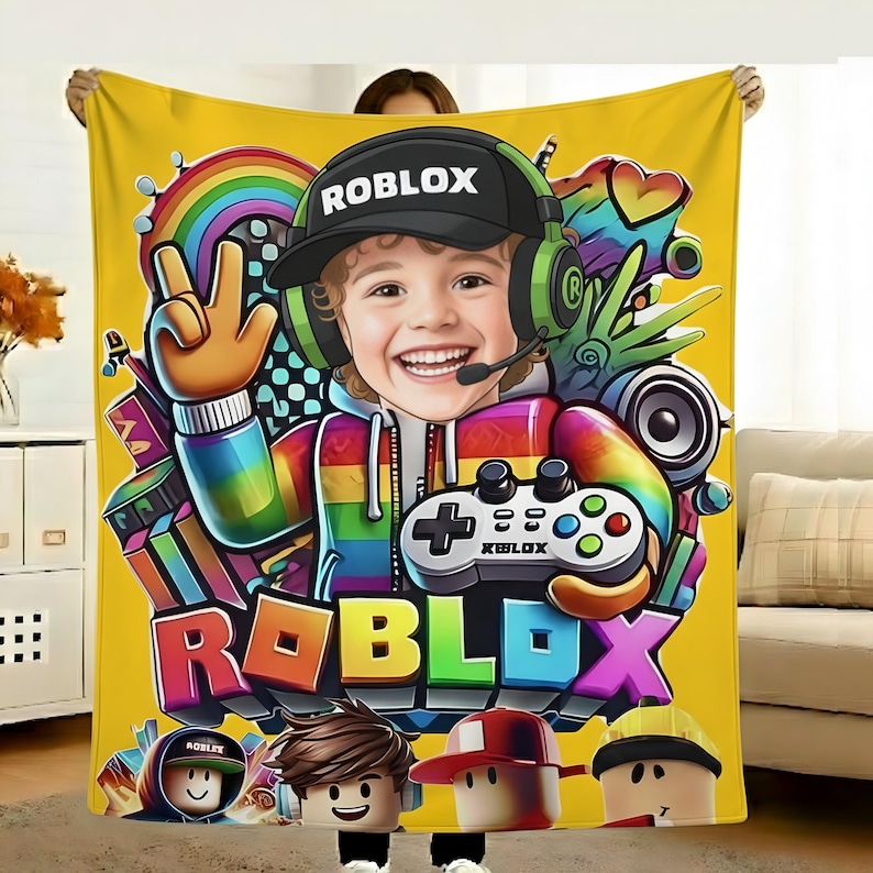 May include: Yellow Roblox-themed blanket featuring a smiling cartoon character wearing a black cap with "ROBLOX" text, headphones, and a rainbow-striped hoodie. The blanket includes a game controller and the Roblox logo.