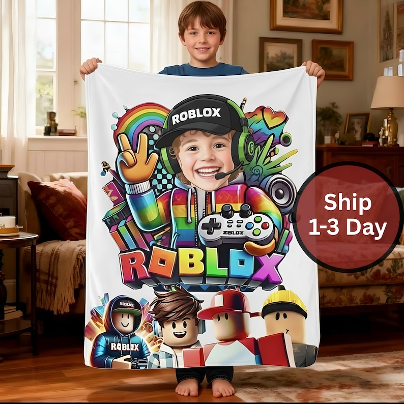 May include: White blanket featuring a colorful Roblox design. The design includes a smiling child wearing a Roblox hat and headset, a rainbow, and the Roblox logo. The blanket is held by a child.