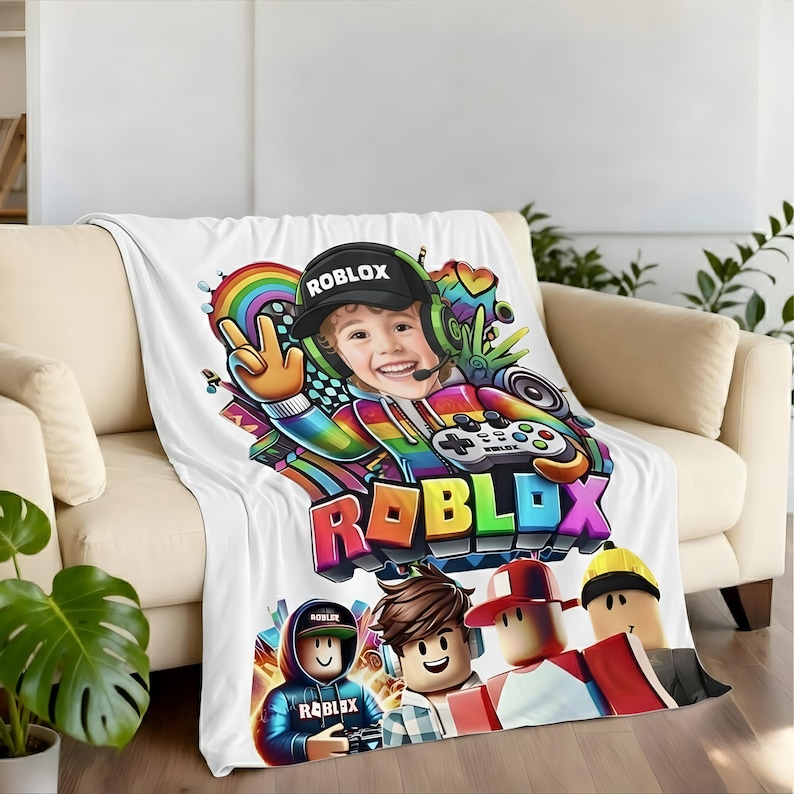 May include: White blanket featuring a colorful graphic of a child wearing a Roblox hat and holding a game controller. The blanket also displays the Roblox logo and several cartoon characters.