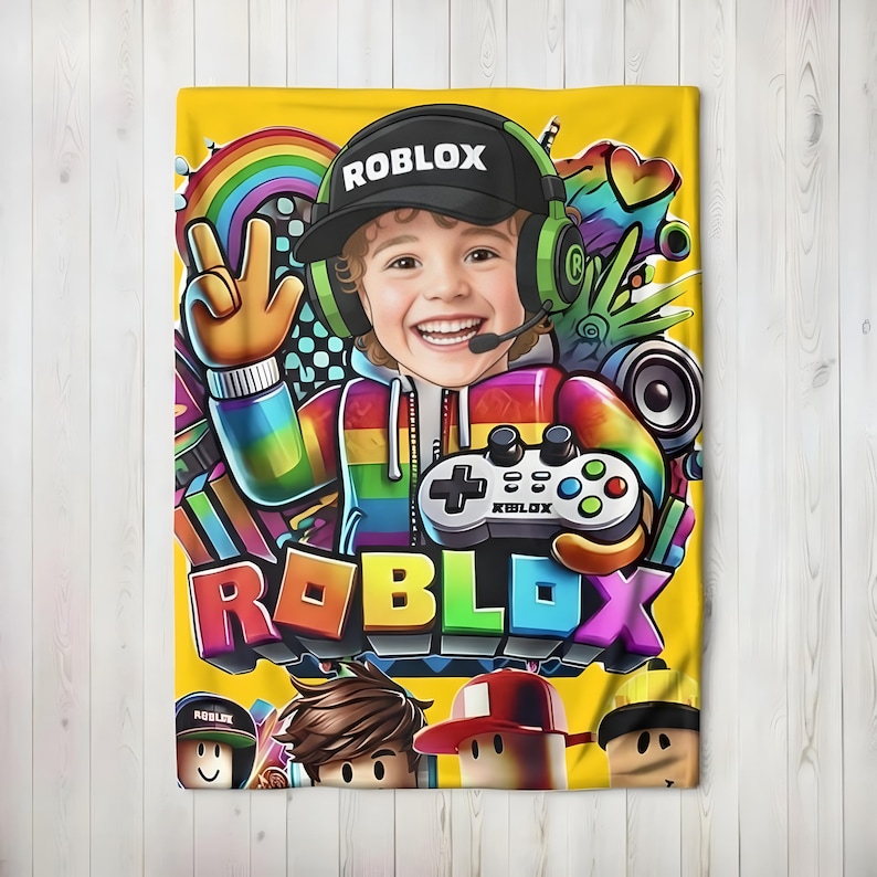 May include: Yellow blanket featuring a colorful graphic of a smiling child wearing a Roblox hat and headset, holding a game controller. The word "ROBLOX" is prominently displayed in 3D letters. A rainbow and other game-related elements complete the design.