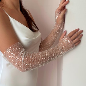 May include: Sheer, fingerless gloves adorned with sequins and beads. The gloves are long, extending up the arm, and are made of a delicate, see-through fabric. The embellishments sparkle, adding a touch of glamour to the accessory.