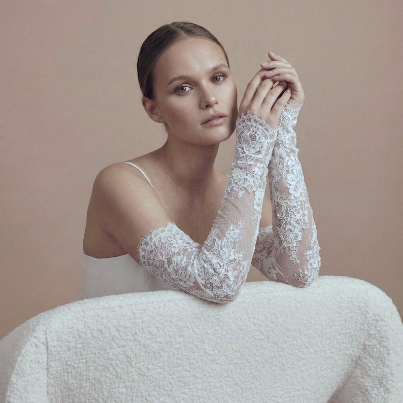 May include: Elegant white lace bridal gloves. The gloves feature intricate floral lace patterns and extend from the wrist to the upper arm. The sheer fabric allows a glimpse of the skin beneath. Perfect for a wedding or special occasion.