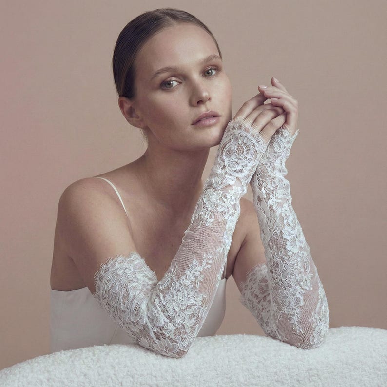 May include: Elegant white lace gloves with intricate floral patterns. The gloves extend from the fingertips to the upper arm, showcasing a delicate and romantic design. Perfect for weddings or special occasions.
