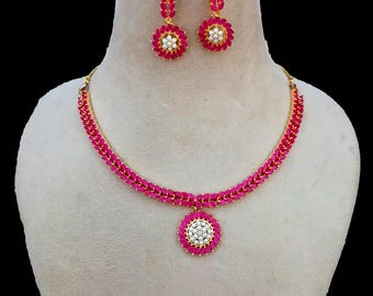 May include: A gold-toned necklace and earring set. The necklace and earrings feature a vibrant pink gemstone design with a central cluster of white stones. The earrings are drop style, and the necklace has a matching pendant.