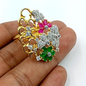 May include: A gold-tone ring featuring an intricate openwork filigree design adorned with clear white stones, a cluster of vibrant pink petal-shaped stones, and a cluster of bright green petal-shaped stones arranged in a floral-inspired pattern.