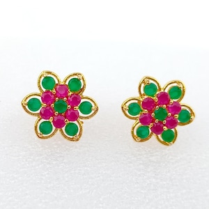 Pode incluir: Um par de brincos de botão dourados em forma de flor. Cada brinco apresenta um grupo central de pedras preciosas rosa rodeadas por pedras preciosas verdes, com um contorno dourado. Os brincos estão sobre um fundo branco.