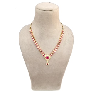 May include: A gold-toned necklace with a series of small, pink gemstones set in a floral pattern. The necklace features a larger, oval-shaped pink gemstone pendant with a teardrop-shaped dangle. The necklace is displayed on a mannequin.