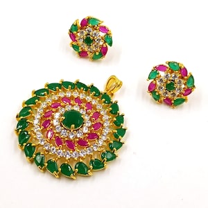 May include: A gold-toned jewelry set consisting of a circular pendant and two matching stud earrings. Each piece features a central green stone surrounded by concentric rings of marquise-cut green and pink stones, accented with clear white crystals.