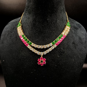 May include: A gold-toned necklace with two strands of alternating white, green, and pink gemstones. A flower pendant with pink and green stones hangs from the bottom strand. The necklace is displayed on a black mannequin.