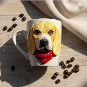May include: White ceramic mug with a sculpted beagle dog face. The dog has yellow fur, brown eyes, and a black nose. It wears a red bandana with white polka dots. Coffee beans are scattered around the mug.