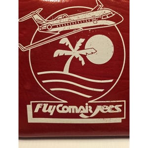 May include: Red square with a white graphic of an airplane, palm tree, sun, and ocean waves. The text "Fly Comair Jets" is at the bottom. The airplane has the word "Comair" on the side.