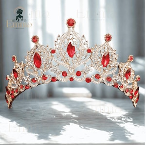 May include: A gold-toned tiara featuring intricate metal filigree work, embellished with numerous clear white rhinestones and several prominent, marquise-cut and round-cut red crystals arranged in a symmetrical, ornate, and pointed crown design.