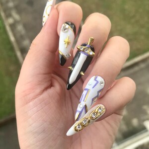 Puede incluir: U&ntilde;as postizas en forma de estilete con una paleta de colores blanco y negro con detalles dorados. Los dise&ntilde;os incluyen un dije de espada en 3D, un emblema de estrella dorada, patrones de l&iacute;neas geom&eacute;tricas moradas y pedrer&iacute;a incrustada.
