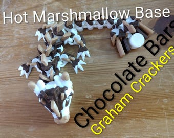 May include: An overhead shot of a dessert creation on a wooden surface. The dessert is shaped like a lizard, made with white, brown, and tan elements. The text "Hot Marshmallow Base" and "Chocolate Graham Crackers" are also visible.