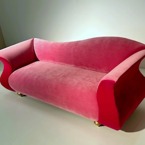 May include: A pink velvet sofa with a curved back and armrests. The sofa has a two-tone design, with a lighter pink on the seat and a darker pink on the arms. The sofa is approximately 183 cm long.