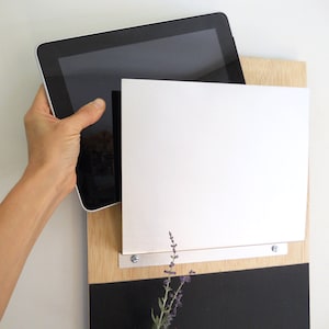 May include: A black tablet computer is propped up against a wooden board with a white dry erase board attached. The board is mounted on a black chalkboard.
