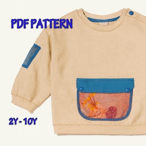 以下が含まれることがあります： 青いアクセントとポケットが付いたベージュの長袖スウェットシャツ。ポケットには、花の模様が入った赤いメッシュのオーバーレイがあります。「PDF PATTERN」と「2Y-10Y」の文字が画像に表示されています。