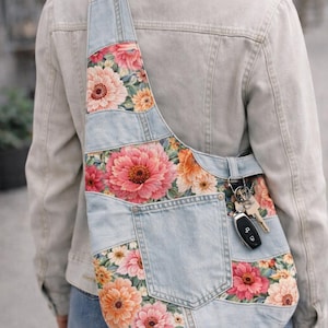 Może przedstawiać: Dżinsowa torba na ramię z kwiatowym wzorem z różowymi, pomarańczowymi i żółtymi kwiatami. Torba ma kieszeń i pasek wykonany z dżinsu. Klucze wiszą na pasku.