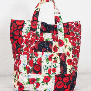 May include: A patchwork tote bag with a floral poppy design. The bag features a variety of fabric squares in red, black, white, and cream, with poppy and floral patterns. The bag has two handles.