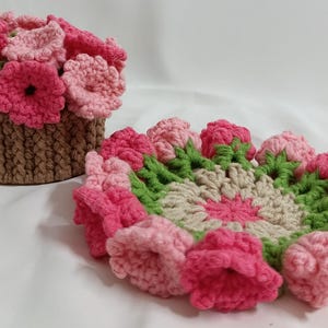May include: Handmade crochet flower basket and coaster set. The basket is brown with pink and light pink flowers. The coaster has a floral design with pink, green, and beige colors. The set is made of yarn.