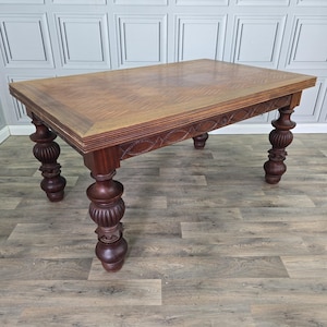 May include: A rectangular wooden dining table featuring a parquet top with a geometric pattern. The table has a dark brown finish and is supported by four thick, turned legs with a bulbous, fluted design. The apron displays a carved oval motif.