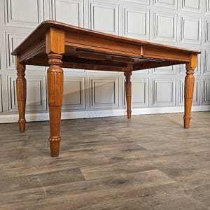 May include: A rectangular wooden dining table in a warm, honey colour. It has ornate, carved legs and a smooth tabletop. The design suggests a classic, traditional style, suitable for a dining room or kitchen. The table's dimensions are not visible, but it is likely over 100 cm in length.