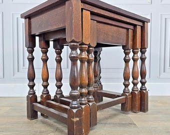 May include: Set of three antique wooden nesting tables. The tables are various sizes, with dark brown tops and intricately carved legs. The tables are nested together, showcasing their graduated sizes and ornate design. The wood has a warm, aged appearance.