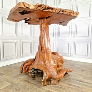 May include: A unique, handcrafted wooden table. The table features a natural, raw-edge tabletop supported by a textured, tree-trunk-shaped base. The table's dimensions are approximately 76 cm in height and 91 cm in width, showcasing a rustic aesthetic.