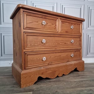 May include: A wooden chest of drawers with four drawers and crystal knobs. The chest is made of light brown wood with a curved top and decorative base. The drawers are arranged in two rows of two, each with a clear crystal knob.